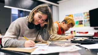 Opiskelija istuu piirtämässä hymyillen.