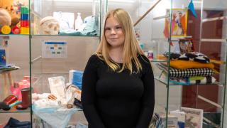Jessi seisoo vitriinin edessä, jossa on sosiaali- ja terveysalan välineistöä.