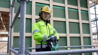 Oskari seisoo talon seunustalla työvaatteissa.