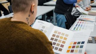 Takaa kuvattu opiskelija selaamassa värikarttoja.