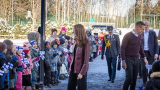 Oppilaiden kunniakuja presidenttiparille. Presidenttipari kävelee keskellä. Oppilailla on Suomen lippuja kädessä.