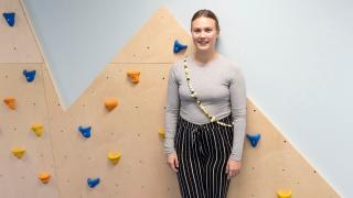 Siiri seisoo hymyillen päiväkodin kiipeilyseinän edessä.