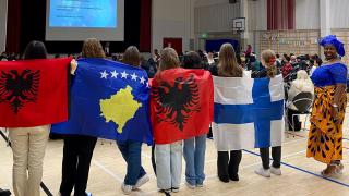 Opiskelijoita eri maiden lippujen kanssa selkäpuolelta kuvattuna Koivukylän salissa.