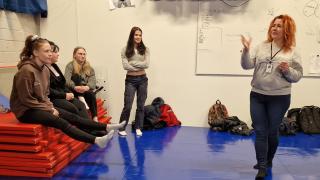 Neljä turvallisuusalan opiskeliaa seuraa kun opettaja Elina Salo ohjeistaa heitä simulaatiossa.