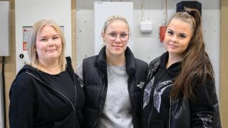 Veera, Ona ja Sini hymyilevät sähköalan opetustiloissa.