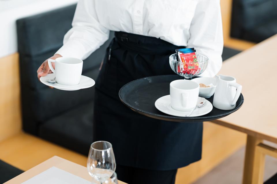 Lähikuva tarjoilijan käsistä, joissa on tarjotin ja kahvikuppeja.